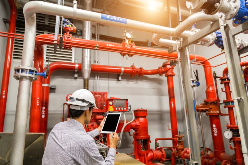 Engineer using a tablet while inspecting a red generator pump